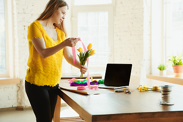 Image showing Florist at work: woman shows how to make bouquet with tulips, working at home concept, using ribbons