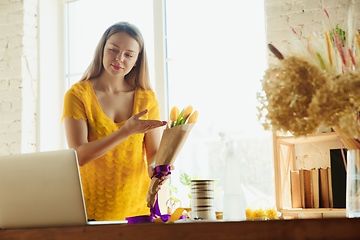 Image showing Florist at work: woman shows how to make bouquet with tulips, working at home concept, preparing flowers