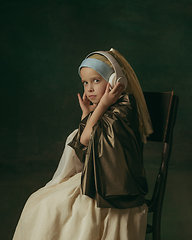 Image showing Medieval little girl as a lady with a pearl earring on dark studio background. Concept of comparison of eras, childhood. Stylish creative design, art vision, new look of artwork.