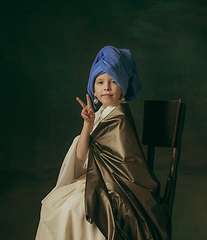 Image showing Medieval little girl as a lady with a pearl earring on dark studio background. Concept of comparison of eras, childhood. Stylish creative design, art vision, new look of artwork.