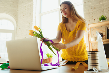 Image showing Florist at work: woman shows how to make bouquet with tulips, working at home concept, preparing flowers