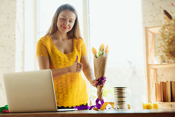 Image showing Florist at work: woman shows how to make bouquet with tulips, working at home concept, thumb up