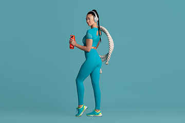 Image showing Beautiful young female athlete practicing on blue studio background, monochrome portrait