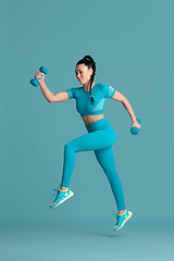 Image showing Beautiful young female athlete practicing on blue studio background, monochrome portrait