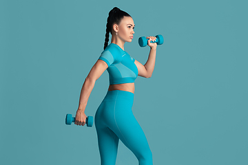 Image showing Beautiful young female athlete practicing on blue studio background, monochrome portrait