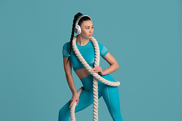 Image showing Beautiful young female athlete practicing on blue studio background, monochrome portrait