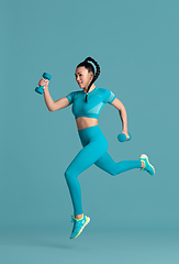 Image showing Beautiful young female athlete practicing on blue studio background, monochrome portrait