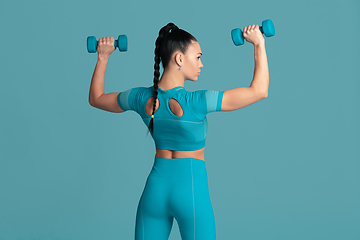 Image showing Beautiful young female athlete practicing on blue studio background, monochrome portrait