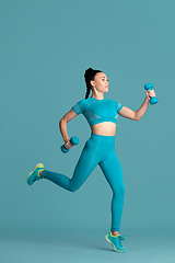 Image showing Beautiful young female athlete practicing on blue studio background, monochrome portrait