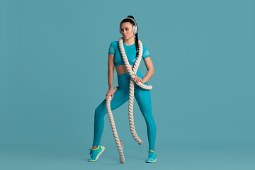 Image showing Beautiful young female athlete practicing on blue studio background, monochrome portrait