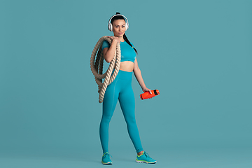 Image showing Beautiful young female athlete practicing on blue studio background, monochrome portrait