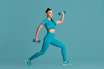 Image showing Beautiful young female athlete practicing on blue studio background, monochrome portrait