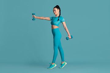 Image showing Beautiful young female athlete practicing on blue studio background, monochrome portrait