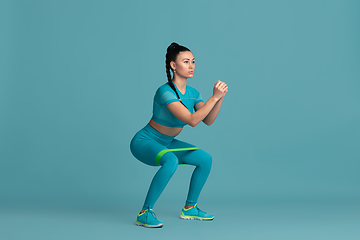 Image showing Beautiful young female athlete practicing on blue studio background, monochrome portrait