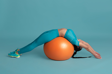 Image showing Beautiful young female athlete practicing on blue studio background, monochrome portrait