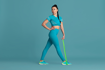 Image showing Beautiful young female athlete practicing on blue studio background, monochrome portrait