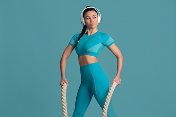 Image showing Beautiful young female athlete practicing on blue studio background, monochrome portrait