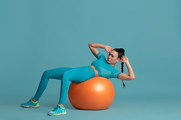 Image showing Beautiful young female athlete practicing on blue studio background, monochrome portrait