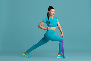 Image showing Beautiful young female athlete practicing on blue studio background, monochrome portrait