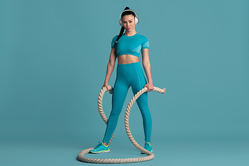 Image showing Beautiful young female athlete practicing on blue studio background, monochrome portrait