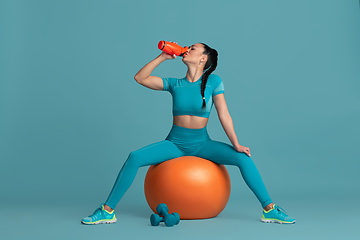 Image showing Beautiful young female athlete practicing on blue studio background, monochrome portrait