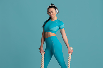 Image showing Beautiful young female athlete practicing on blue studio background, monochrome portrait