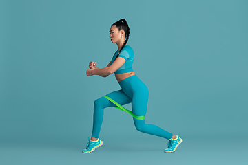 Image showing Beautiful young female athlete practicing on blue studio background, monochrome portrait