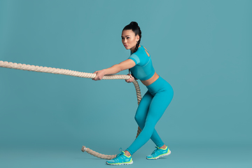 Image showing Beautiful young female athlete practicing on blue studio background, monochrome portrait