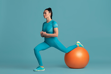 Image showing Beautiful young female athlete practicing on blue studio background, monochrome portrait