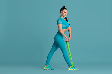 Image showing Beautiful young female athlete practicing on blue studio background, monochrome portrait