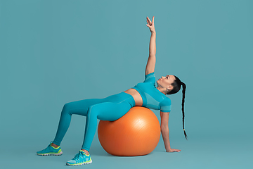 Image showing Beautiful young female athlete practicing on blue studio background, monochrome portrait