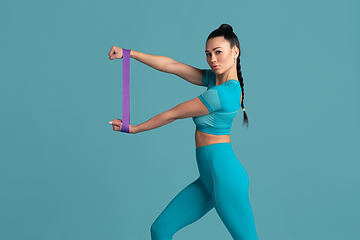 Image showing Beautiful young female athlete practicing on blue studio background, monochrome portrait