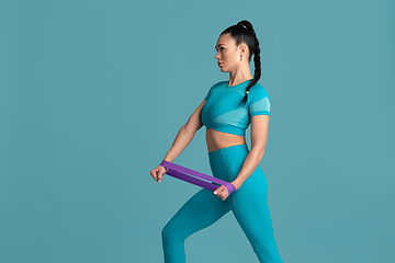 Image showing Beautiful young female athlete practicing on blue studio background, monochrome portrait