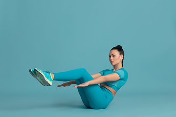 Image showing Beautiful young female athlete practicing on blue studio background, monochrome portrait