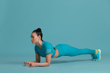 Image showing Beautiful young female athlete practicing on blue studio background, monochrome portrait