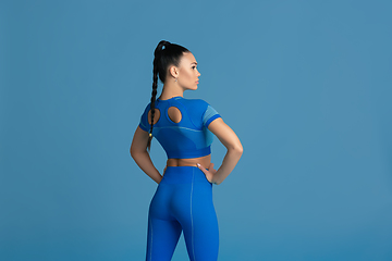 Image showing Beautiful young female athlete practicing on blue studio background, monochrome portrait