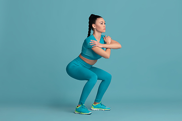 Image showing Beautiful young female athlete practicing on blue studio background, monochrome portrait