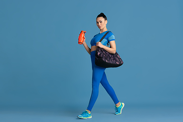 Image showing Beautiful young female athlete practicing on blue studio background, monochrome portrait