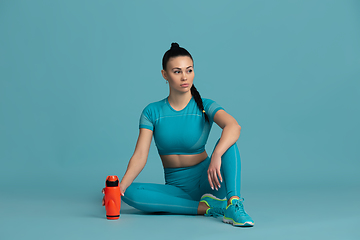 Image showing Beautiful young female athlete practicing on blue studio background, monochrome portrait