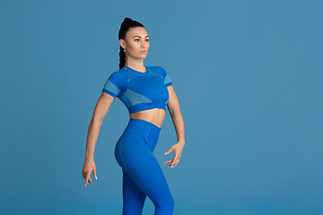 Image showing Beautiful young female athlete practicing on blue studio background, monochrome portrait