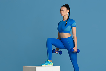 Image showing Beautiful young female athlete practicing on blue studio background, monochrome portrait