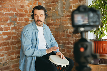 Image showing Caucasian musician playing hand drum during online concert at home isolated and quarantined, inspired improvising