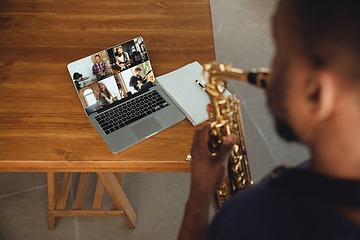 Image showing African-american musician playing saxophone during online concert or sound-check connected with the band at home isolated and quarantined