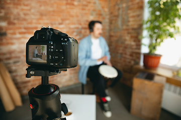 Image showing Caucasian musician playing hand drum during online concert at home isolated and quarantined, focus on camera