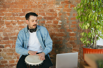 Image showing Caucasian musician playing hand drum during online concert at home isolated and quarantined, inspired improvising