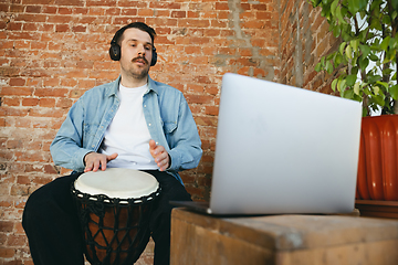 Image showing Caucasian musician playing hand drum during online concert at home isolated and quarantined, improvising