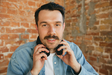 Image showing Caucasian musician in headphones greeting audience before online concert at home isolated and quarantined, cheerful, smiling