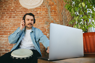 Image showing Caucasian musician playing hand drum during online concert at home isolated and quarantined, inspired improvising