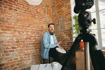 Image showing Caucasian musician playing hand drum during online concert at home isolated and quarantined, concentrated