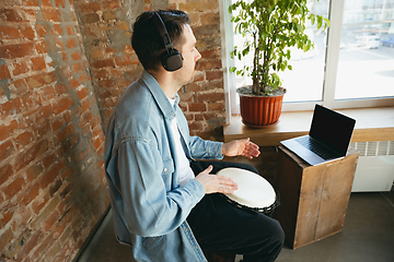 Image showing Caucasian musician playing hand drum during online concert at home isolated and quarantined, improvising